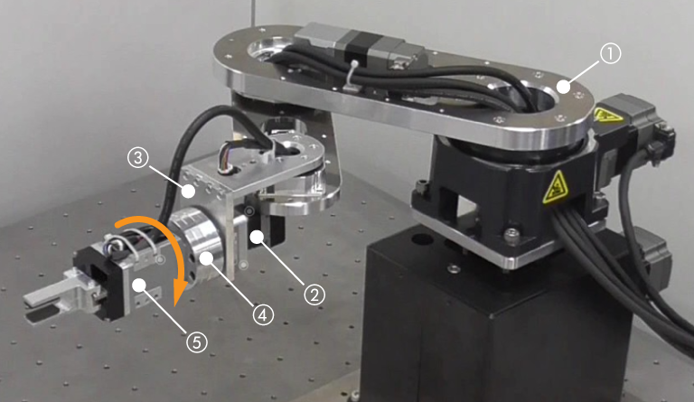 Example of mounting an OVR robot combined with a compact electric cylinder and an electric gripper. Photograph showing the picking operation of a blue cylindrical workpiece. Numbered labels show the mounting positions of each component